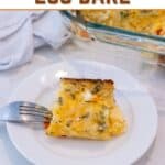 A slice of cheesy egg bake on a white plate with a fork, next to a glass baking dish and a white cloth.