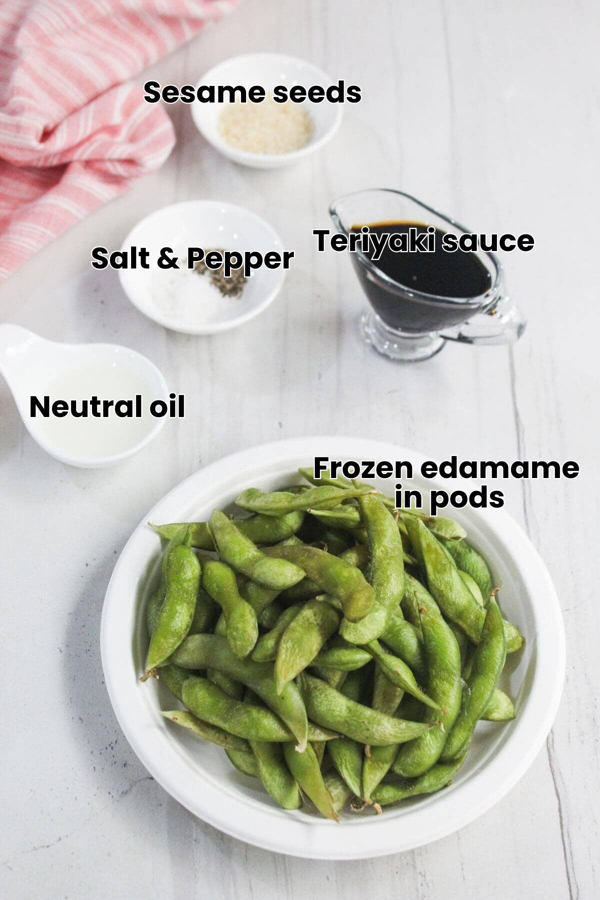 A white bowl of edamame pods is placed on a table next to small bowls of salt, pepper, sesame seeds, vinegar, and a glass container of soy sauce.