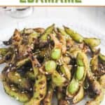 A plate of grilled edamame pods sprinkled with sesame seeds, beneath a sign that reads “Teriyaki Edamame.”.