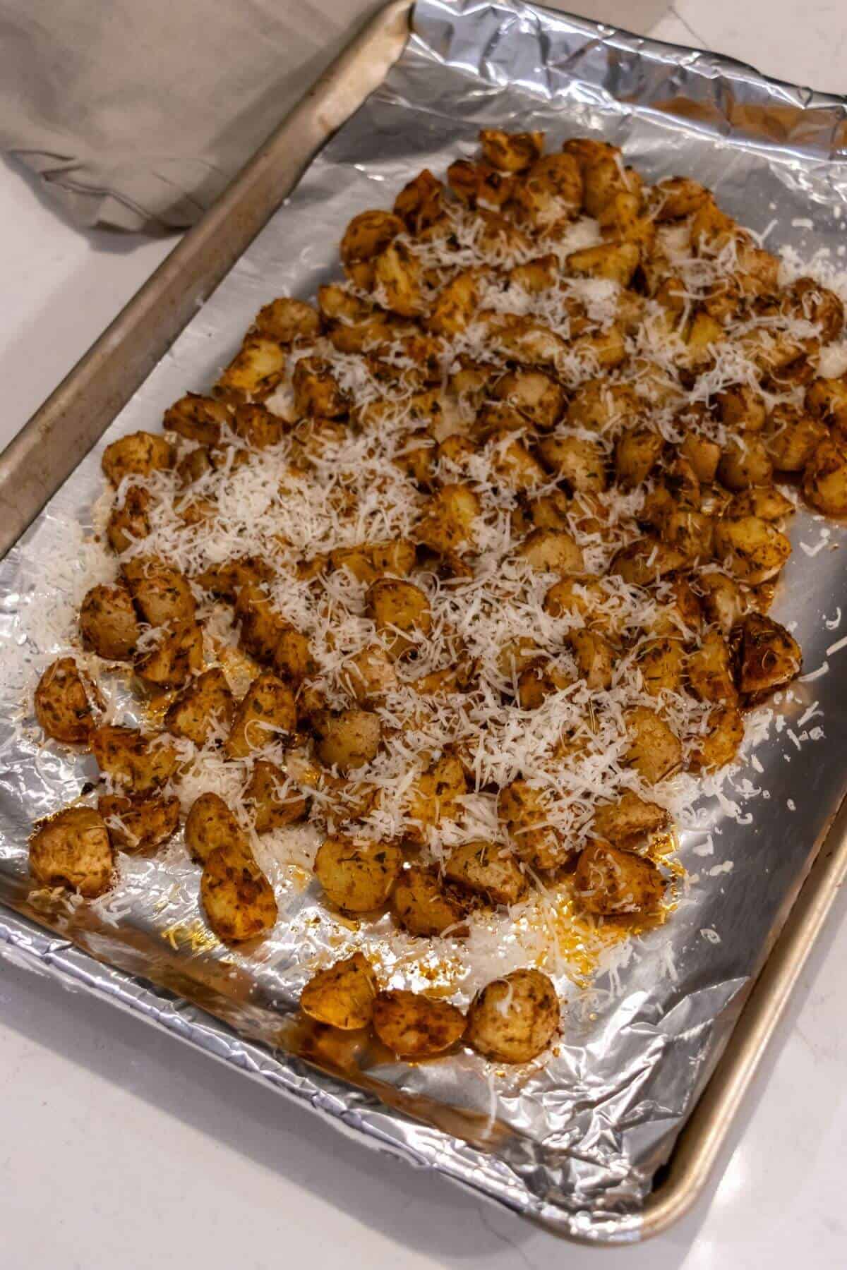 Roasted seasoned potatoes topped with grated cheese on a foil-lined baking sheet.