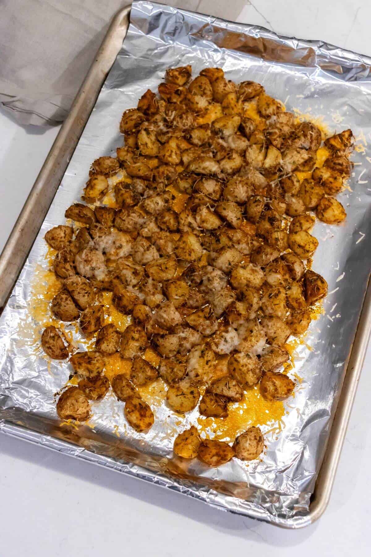 A baking sheet lined with foil holds roasted, seasoned baby potatoes topped with melted cheese.