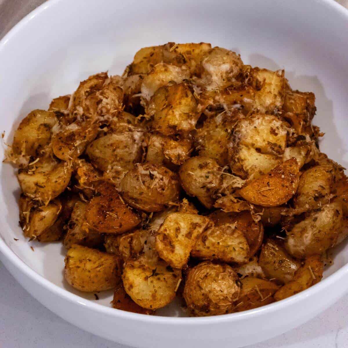 A white bowl filled with roasted potatoes seasoned with herbs and grated cheese.