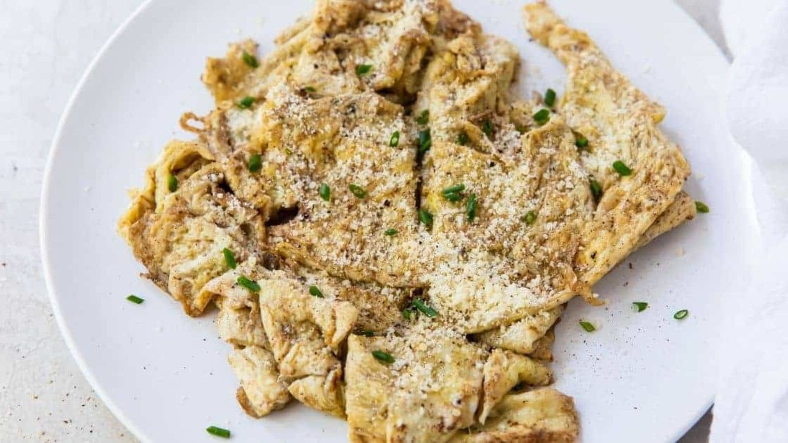 Blackstone Scrambled Eggs with parmesan, chives and bacon on a white plate.