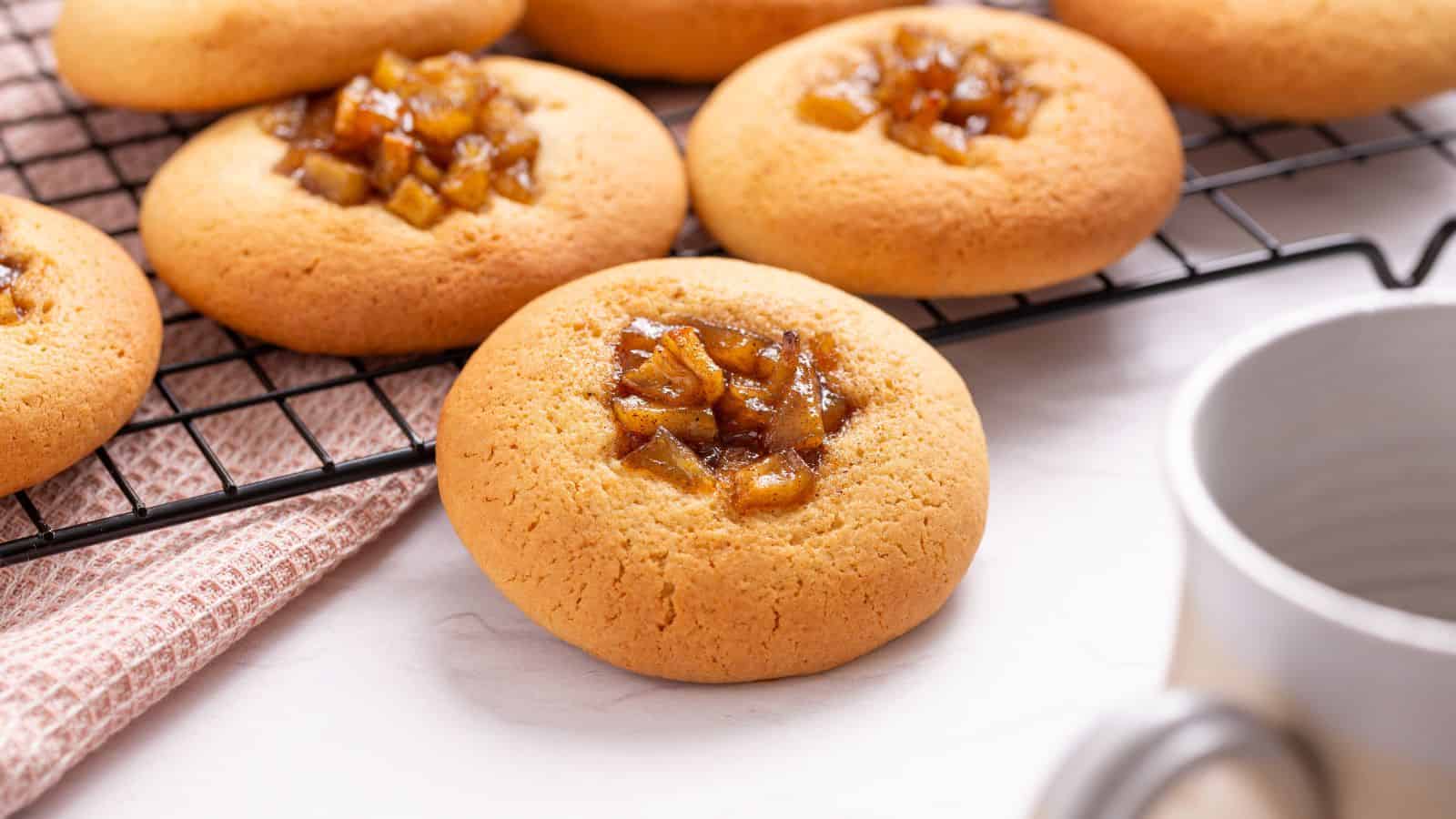Round cookies with a topping of chopped caramelized fruit cooling on a wire rack, with a cup partially visible in the foreground.