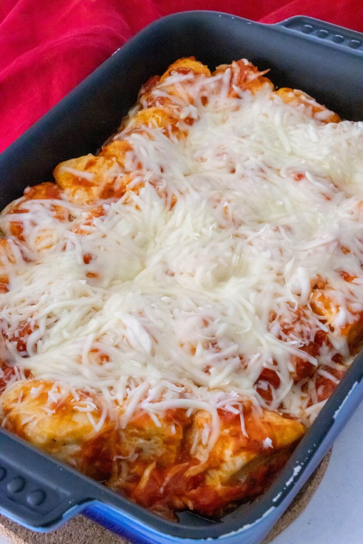A baking dish filled with enchiladas topped with melted cheese and red sauce, placed on a countertop.