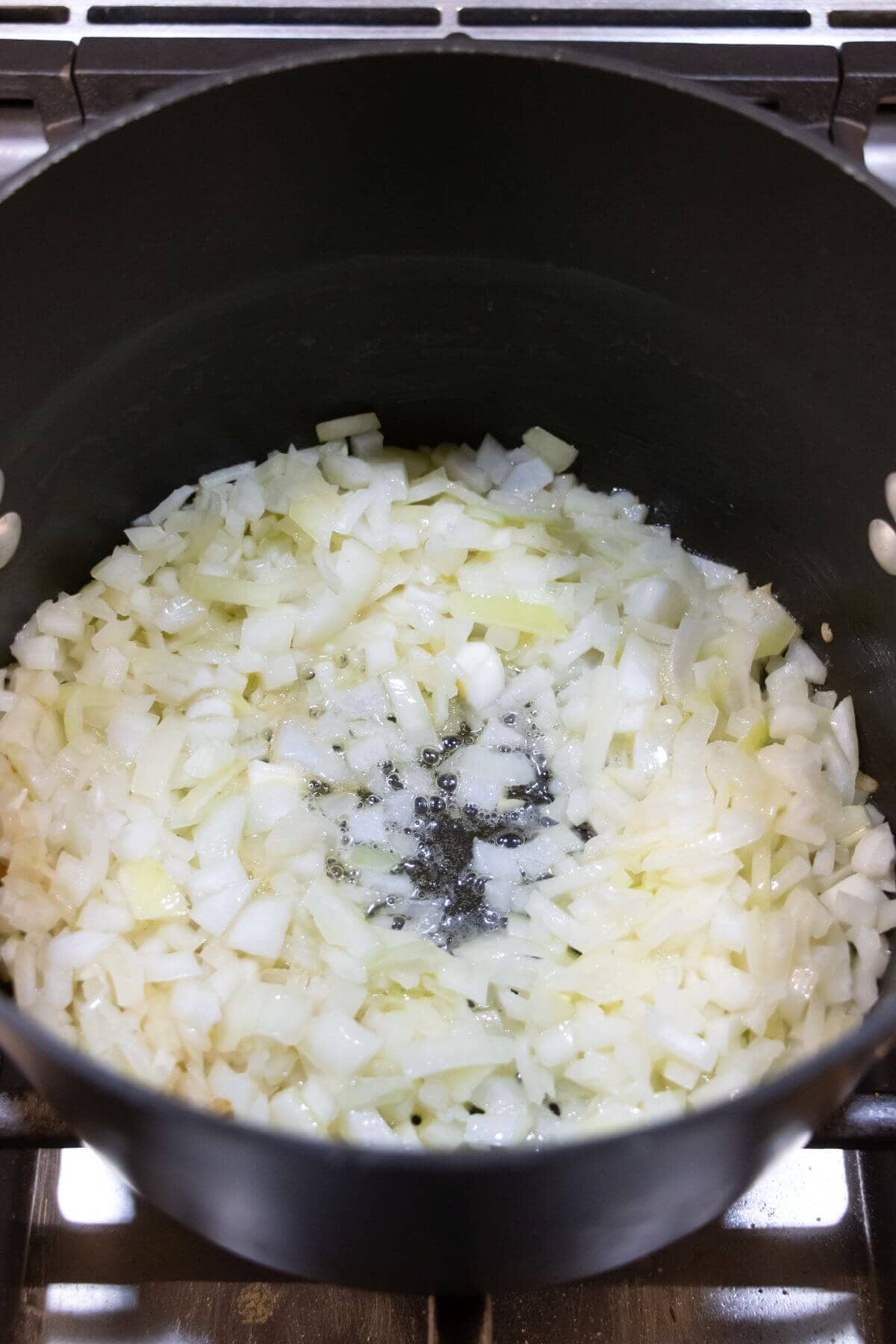 Chopped onions are being sautéed in oil in a black pot on a stove.