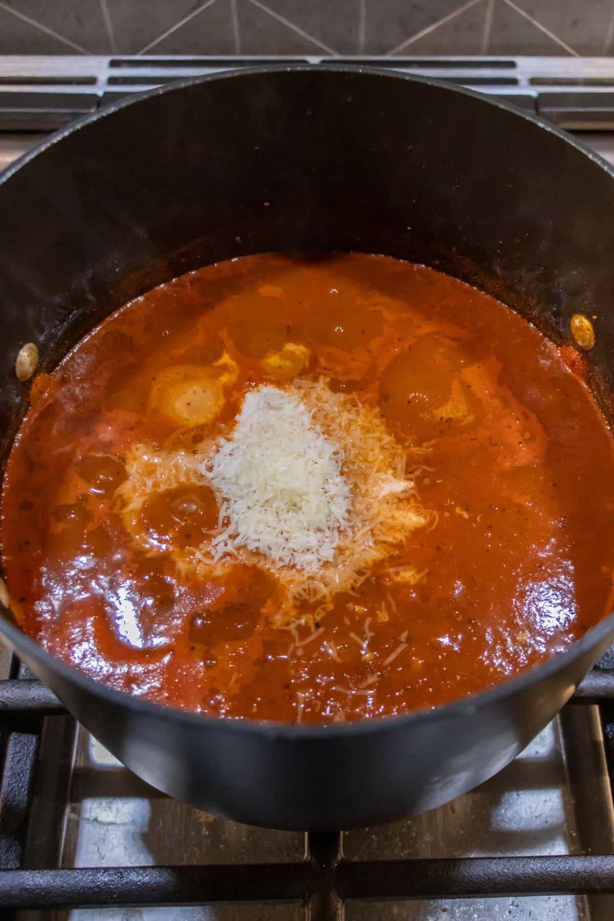 A pot of tomato sauce simmers on a stove, topped with a small mound of grated cheese in the center.