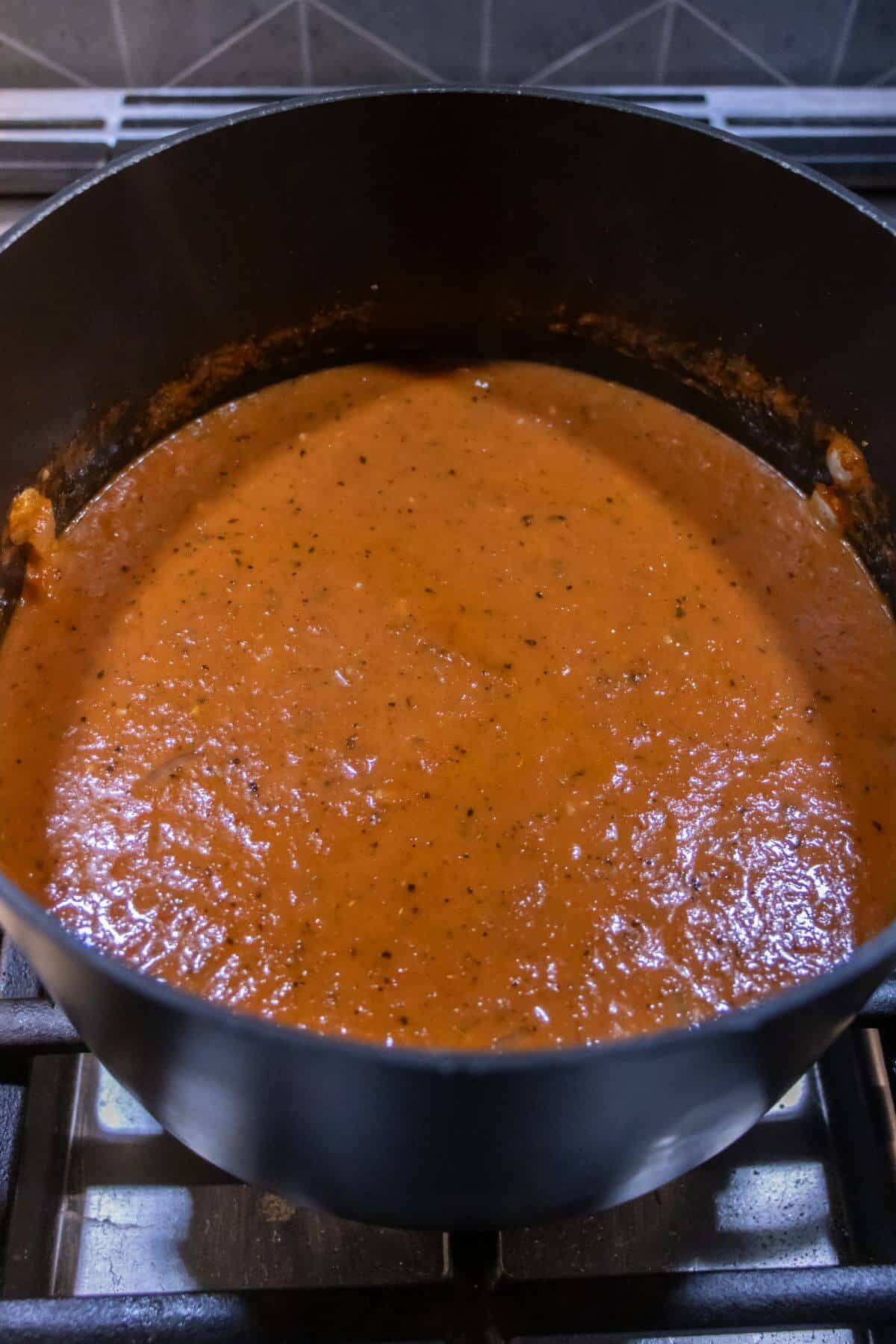 A pot of thick, orange-red tomato sauce with visible herbs simmers on a stovetop.