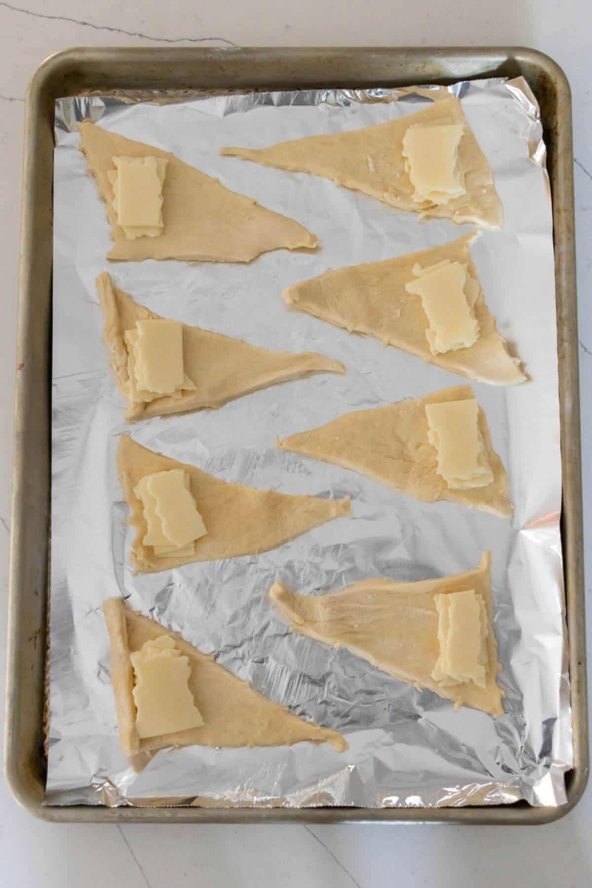 A baking sheet lined with foil holds eight unbaked crescent dough triangles, each topped with a piece of butter.