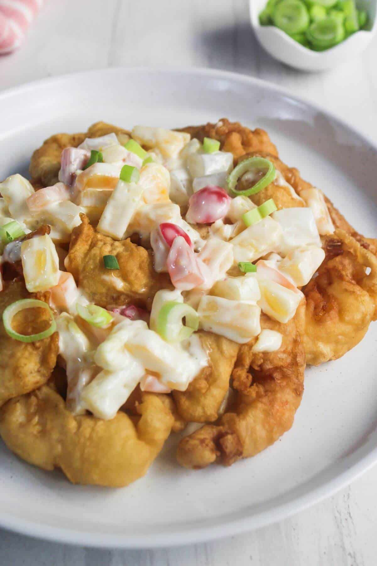A plate of fried dough topped with creamy salad made of chopped vegetables and garnished with sliced green onions.
