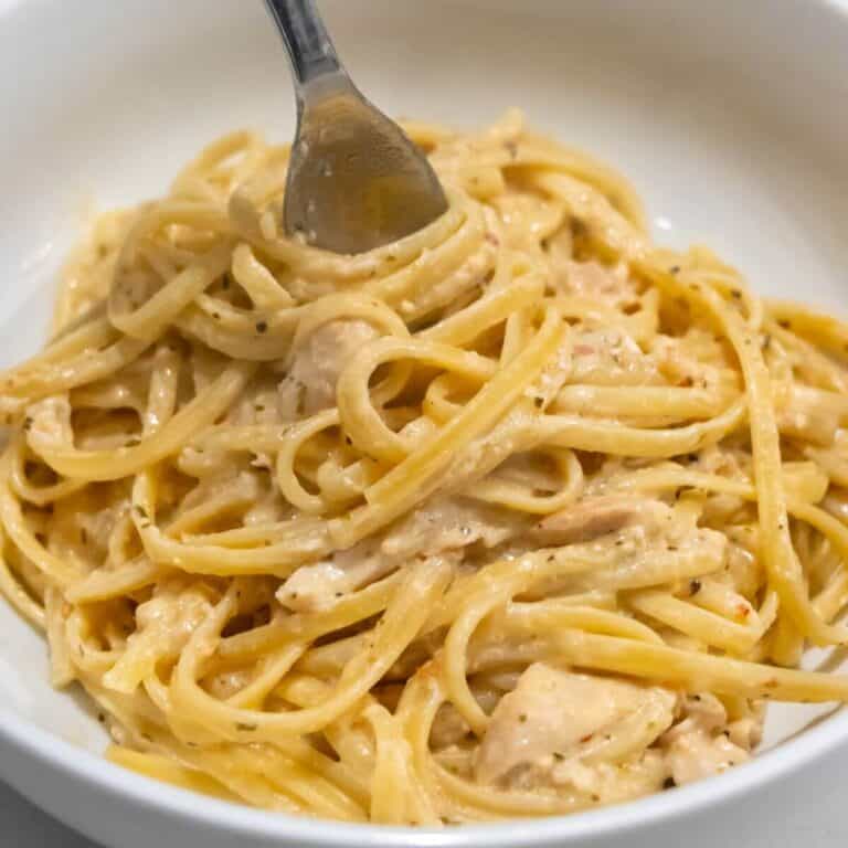 A fork twirls creamy chicken Alfredo pasta in a white bowl.
