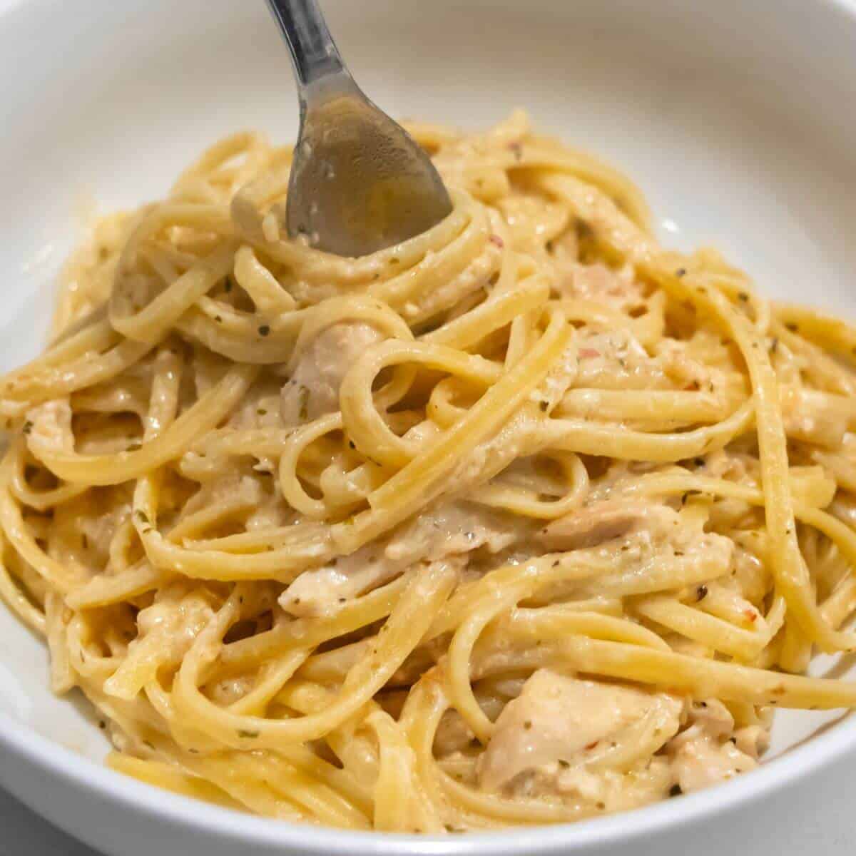 A fork twirls creamy chicken Alfredo pasta in a white bowl.