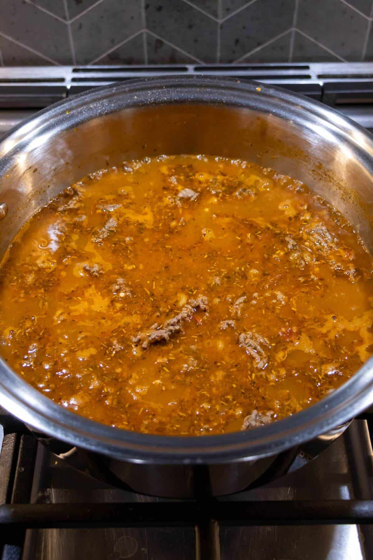 A pot of reddish-brown soup or stew with visible chunks of meat simmering on a stovetop.