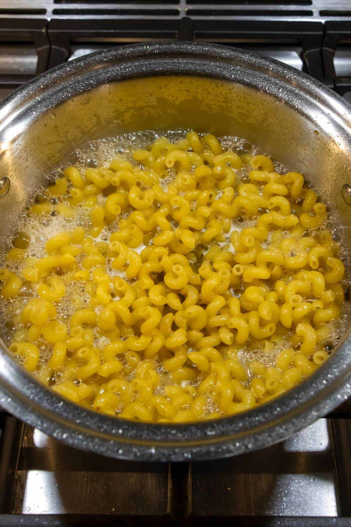 A pot of elbow macaroni pasta boiling in water on a stovetop.