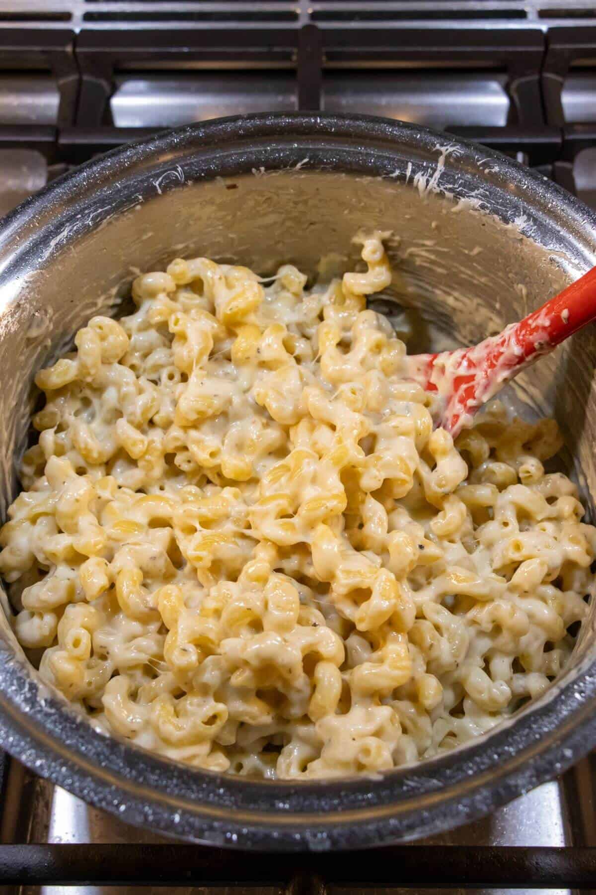 A pot of cooked macaroni and cheese with a red spatula, sitting on a stovetop.