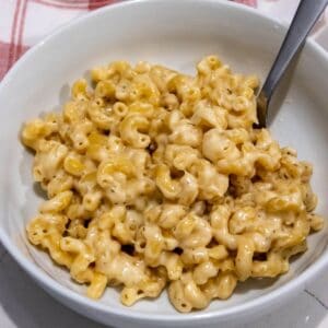 A bowl of creamy macaroni and cheese with a spoon, placed on a white surface.
