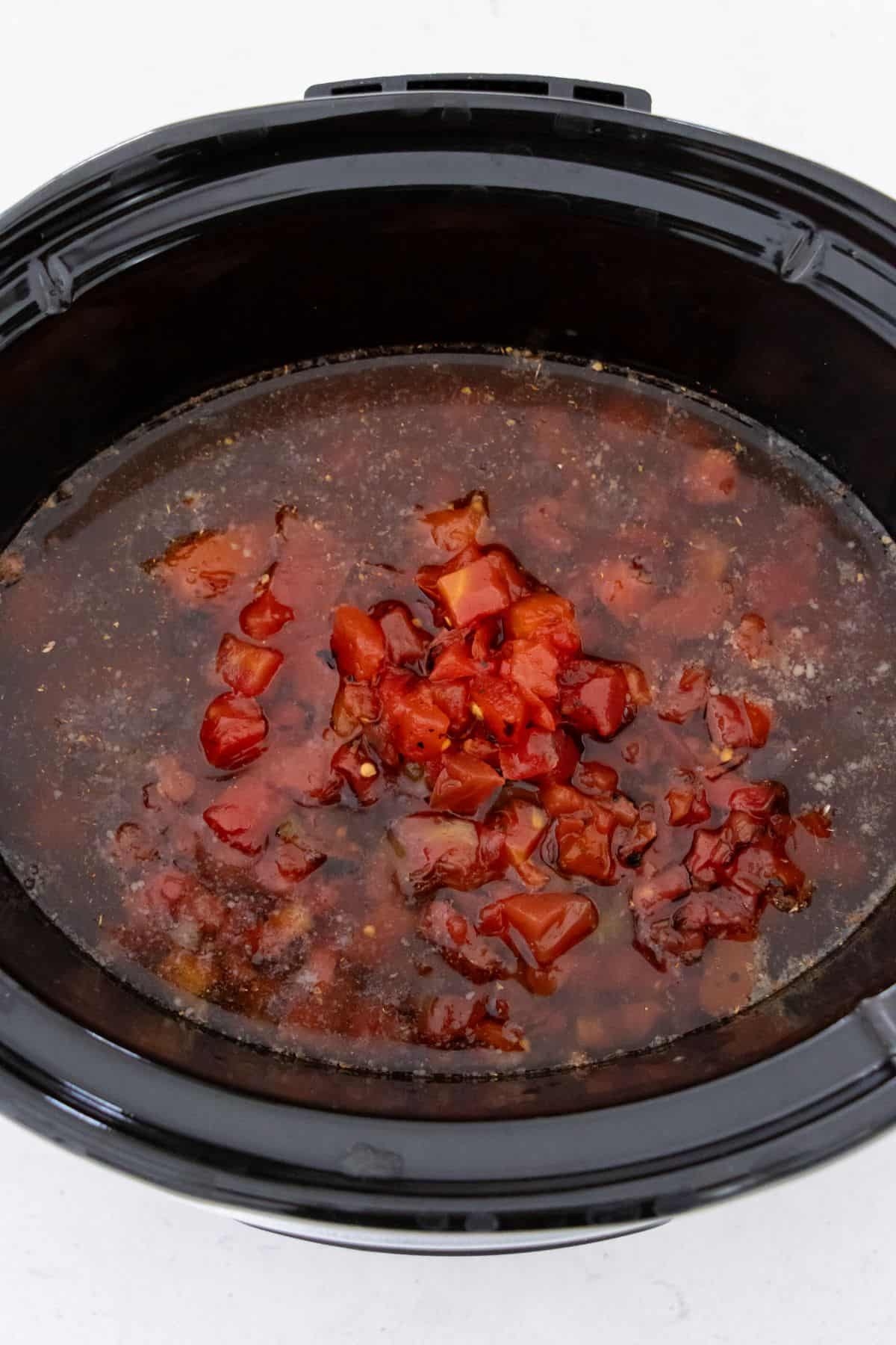 A slow cooker filled with a mixture of chopped tomatoes and broth, in the process of cooking.