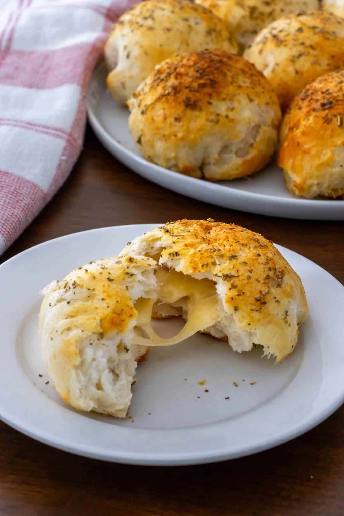 A cheese-stuffed biscuit with a bite taken out sits on a white plate, with a tray of whole biscuits in the background.