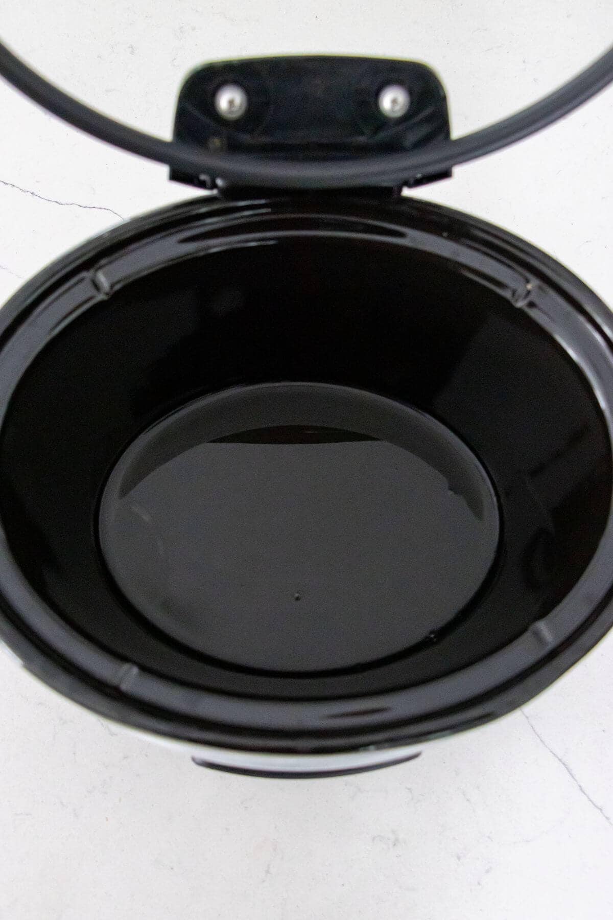 An open black slow cooker with an empty inner pot, viewed from above against a light-colored background.