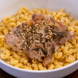 A bowl of macaroni pasta topped with seasoned baked chicken and minced garlic.