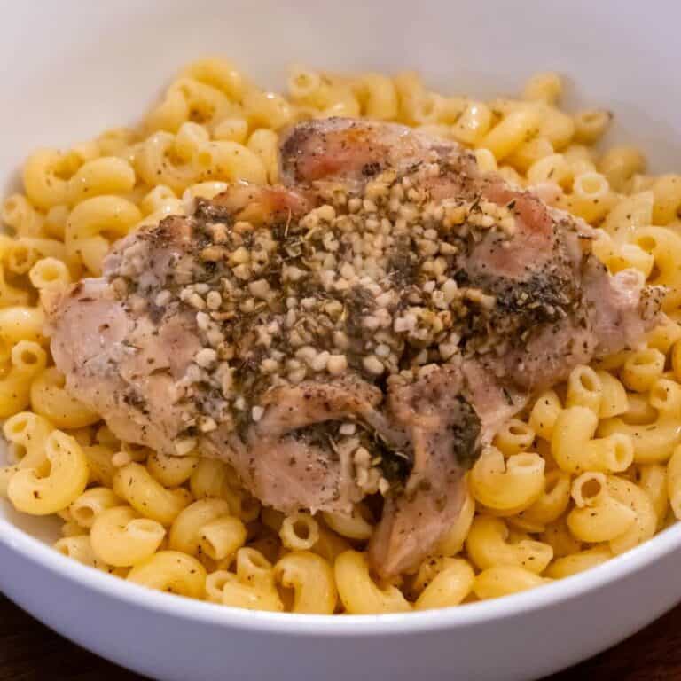 A bowl of macaroni pasta topped with seasoned baked chicken and minced garlic.