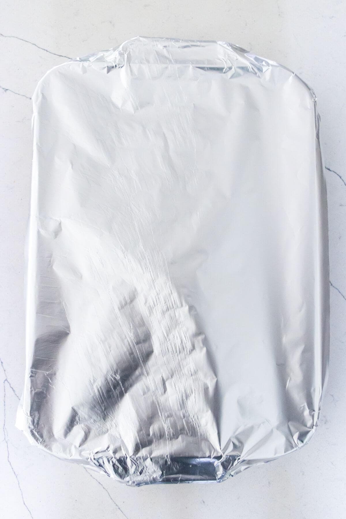 A rectangular baking dish covered with a sheet of aluminum foil sits on a white countertop.
