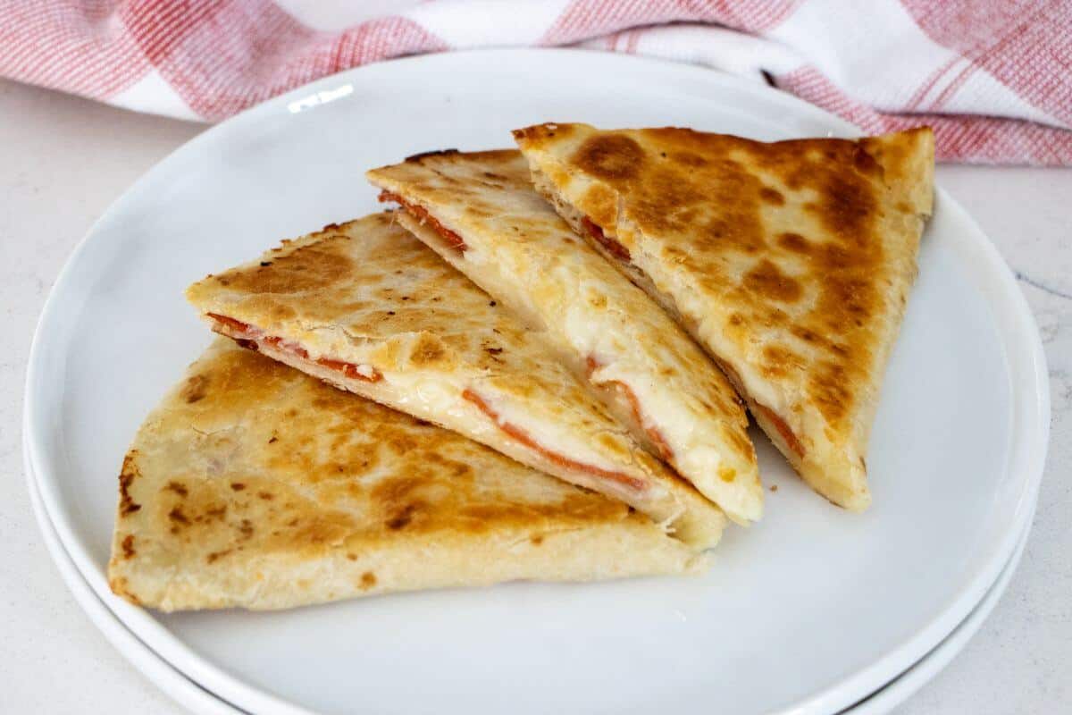 Three triangular slices of a golden-brown quesadilla with melted cheese and pepperoni on a white plate.
