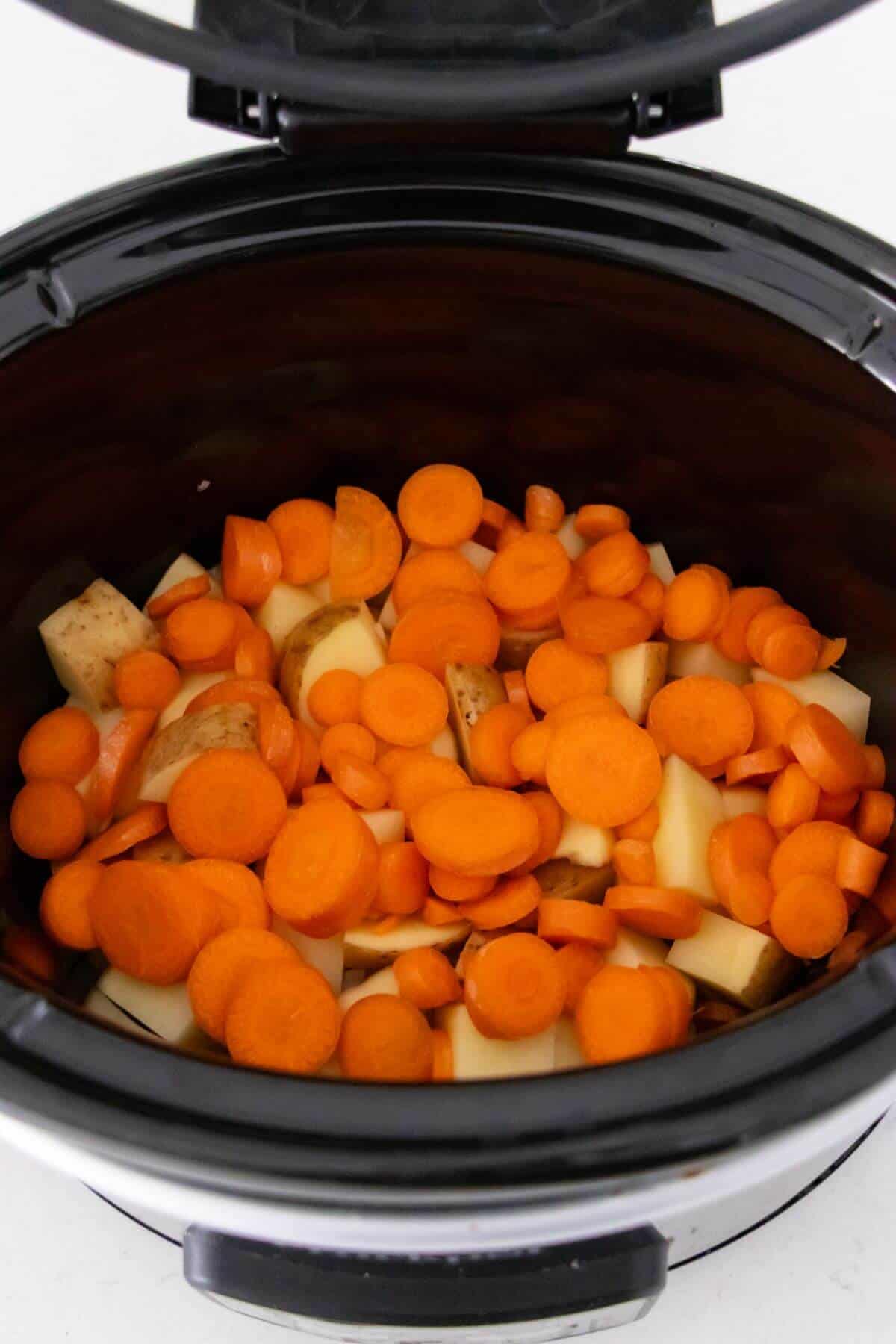 Chopped carrots and potatoes are placed inside a slow cooker, ready for cooking.