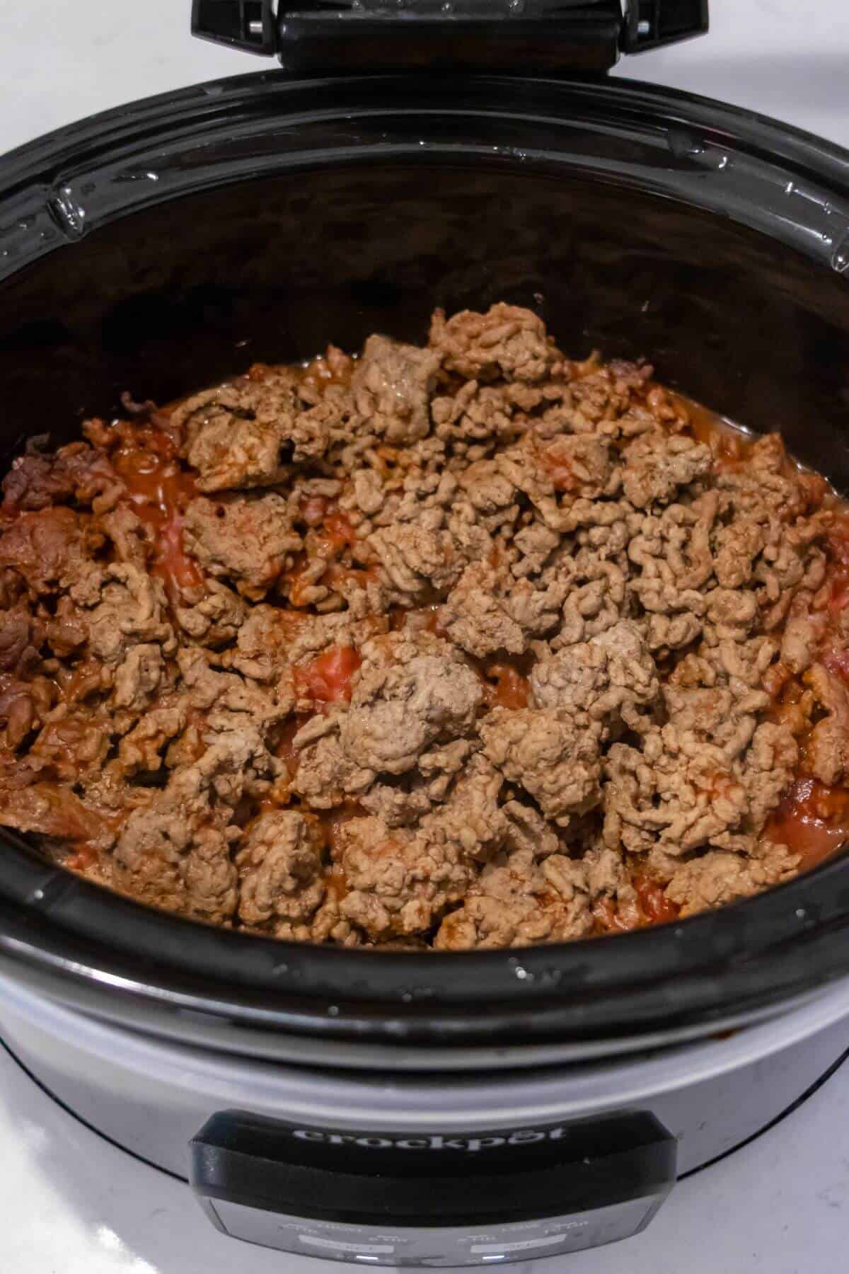 Ground beef cooking in a slow cooker with tomato sauce, viewed from above.