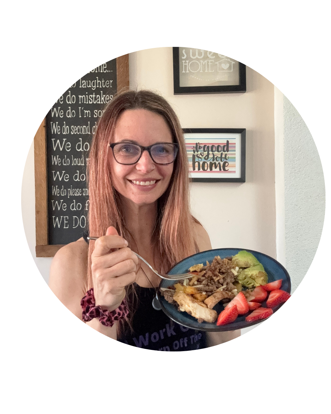Woman with glasses smiles while holding a plate of food with strawberries, rice, avocado, and fried eggs.
