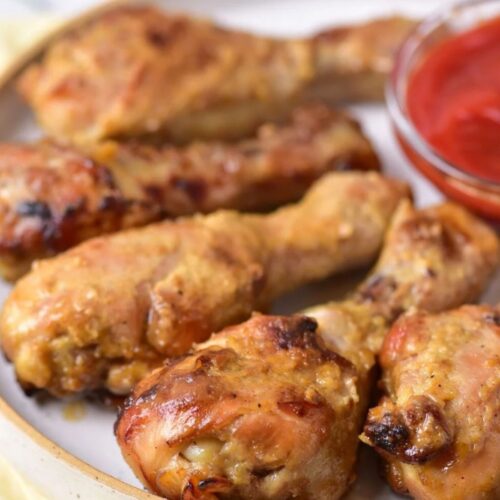 Baked drumsticks on a white plate with ketchup.