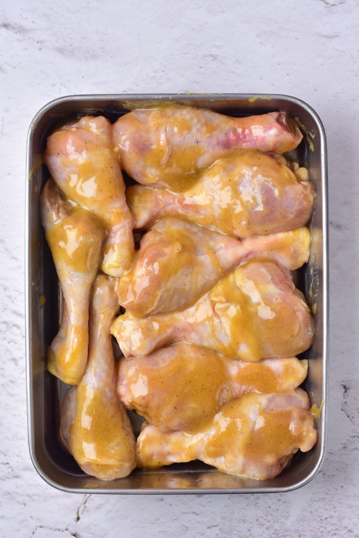 Raw drumsticks in a baking pan with honey mustard sauce on them.