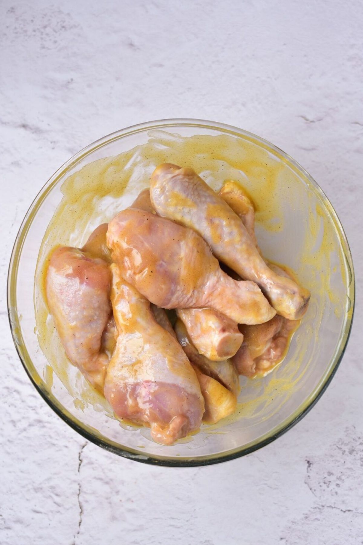 Raw drumsticks in a glass dish with honey mustard sauce on them.