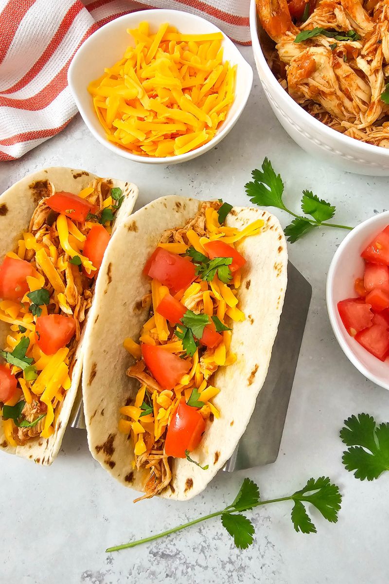 Chicken salsa tacos with tomatoes and cheese and ingredients around them.