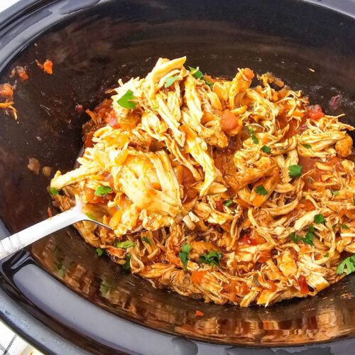 Shredded salsa chicken in a black slow cooker.