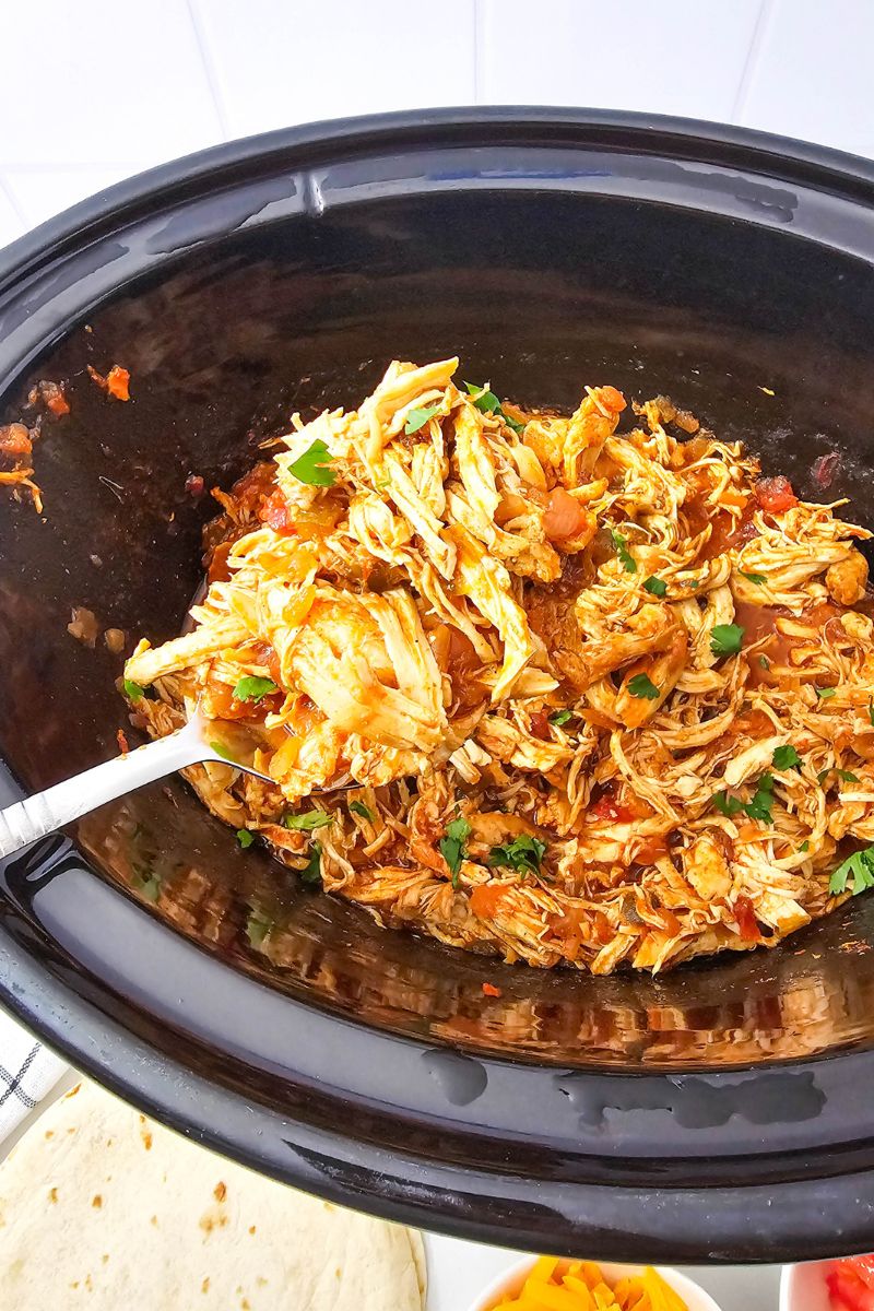 Shredded salsa chicken in a black slow cooker.