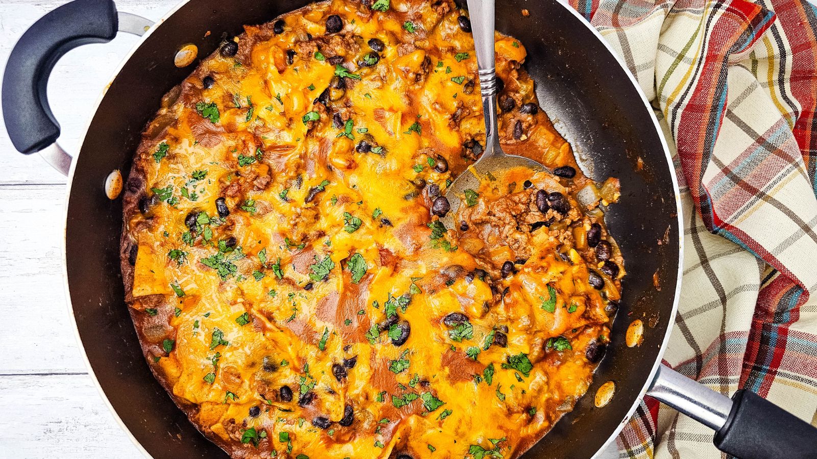 Been enchiladas in a skillet topped with cheese and a spoon in the skillet.