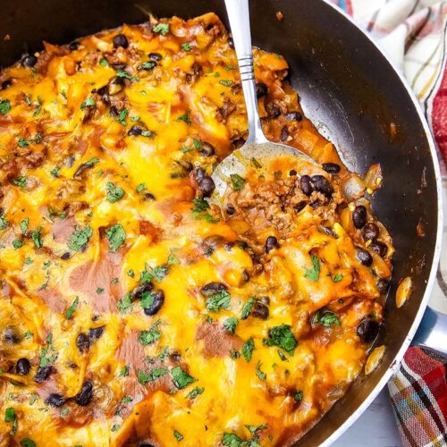 Been enchiladas in a skillet topped with cheese and a spoon in the skillet.