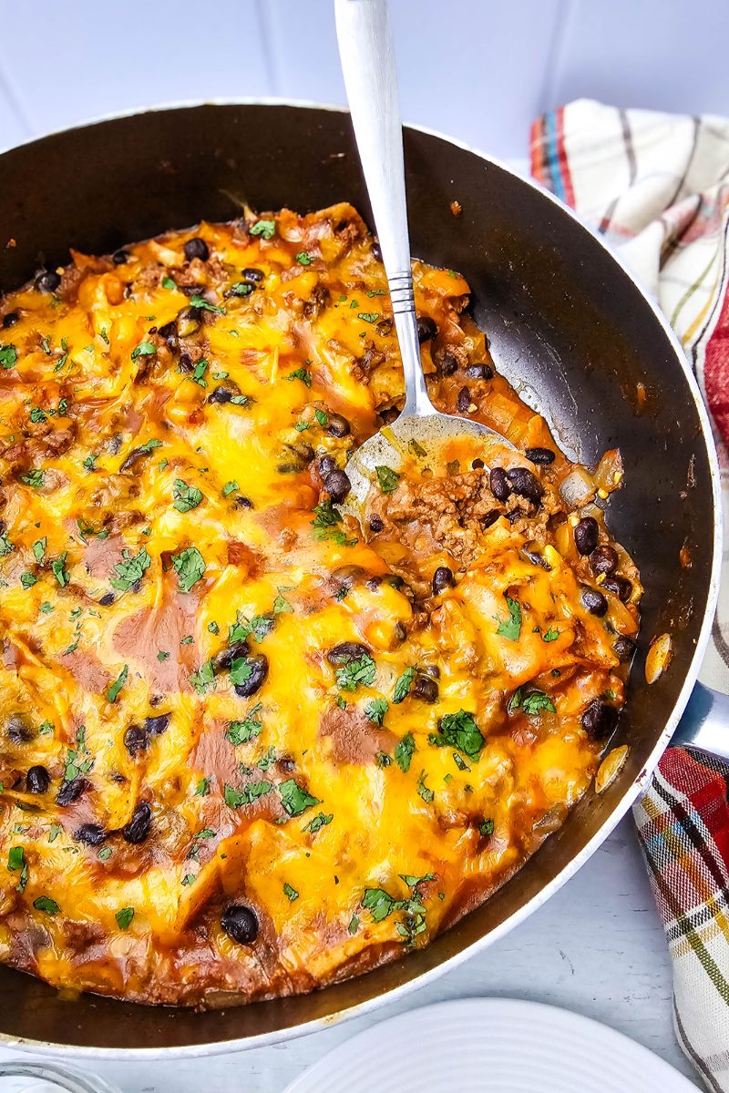 Been enchiladas in a skillet topped with cheese and a spoon in the skillet.