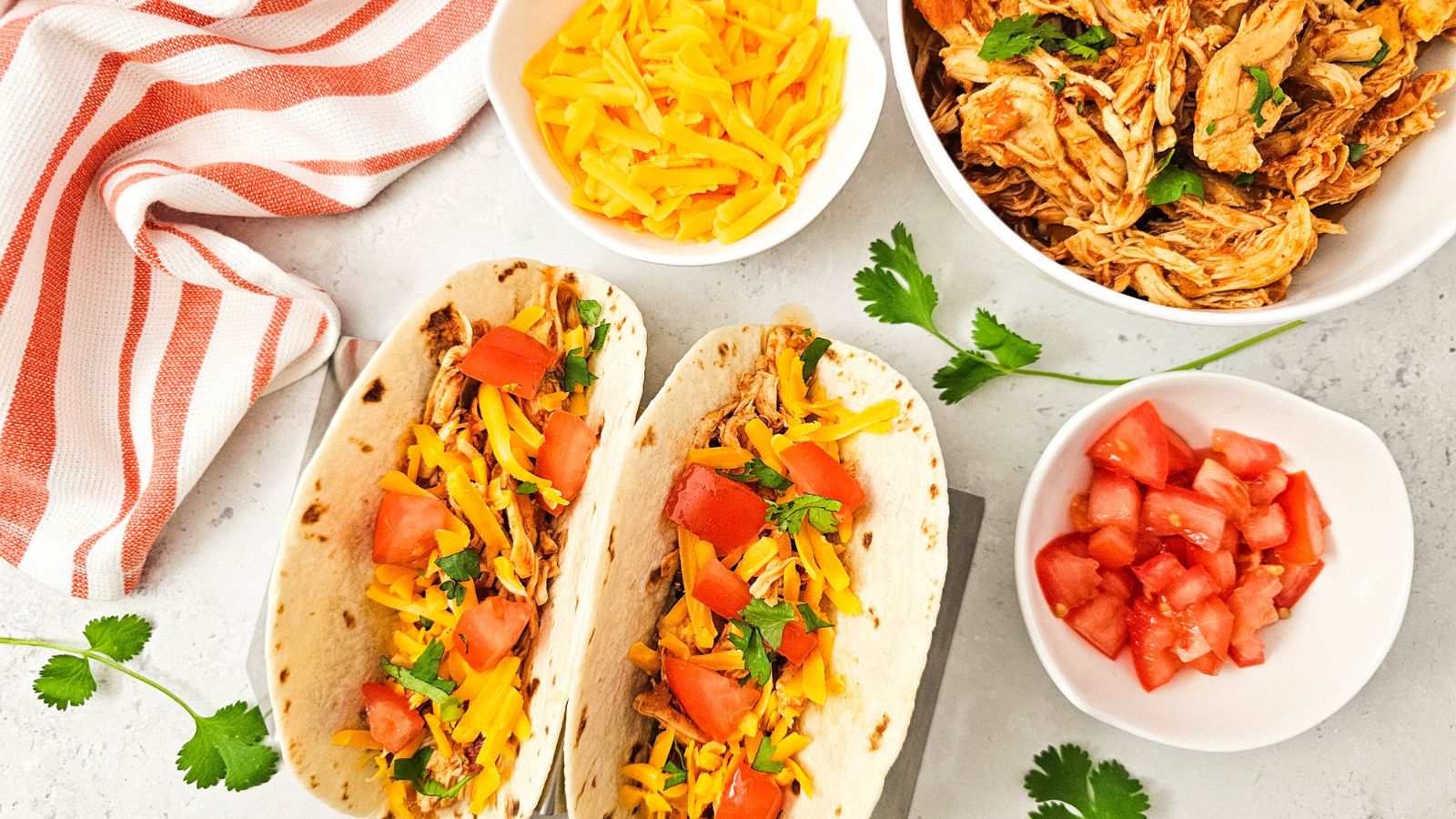 Chicken salsa tacos with tomatoes and cheese and ingredients around them.
