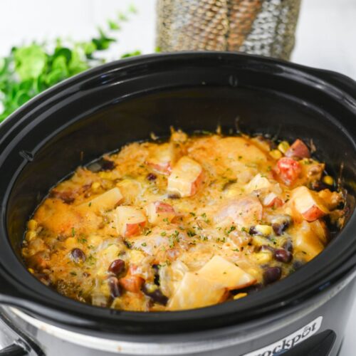 Slow cooker with cowboy casserole topped with cheese in it.