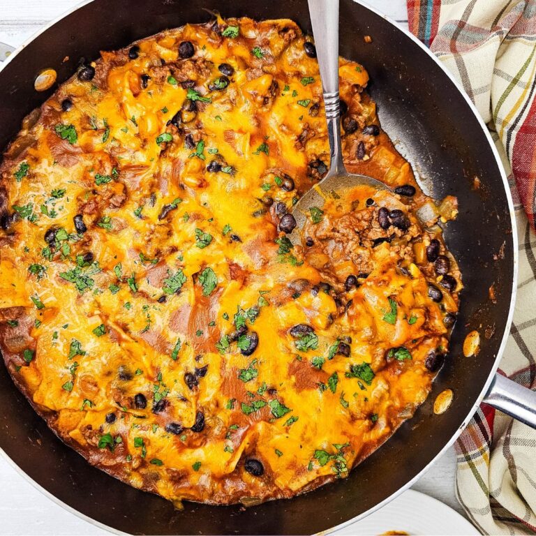Been enchiladas in a skillet topped with cheese and a spoon in the skillet.