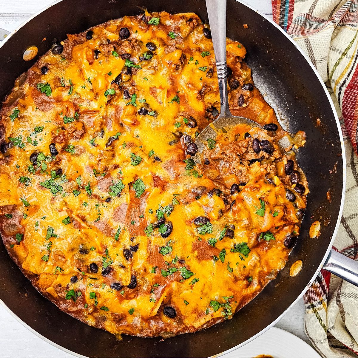 Been enchiladas in a skillet topped with cheese and a spoon in the skillet.