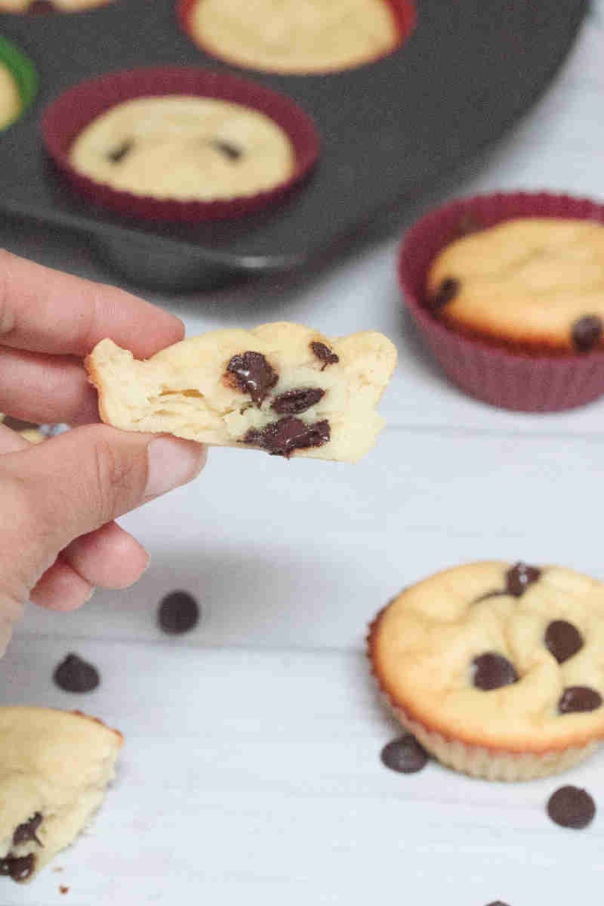 A hand holding up a yogurt, chocolate chip muffin with more around.