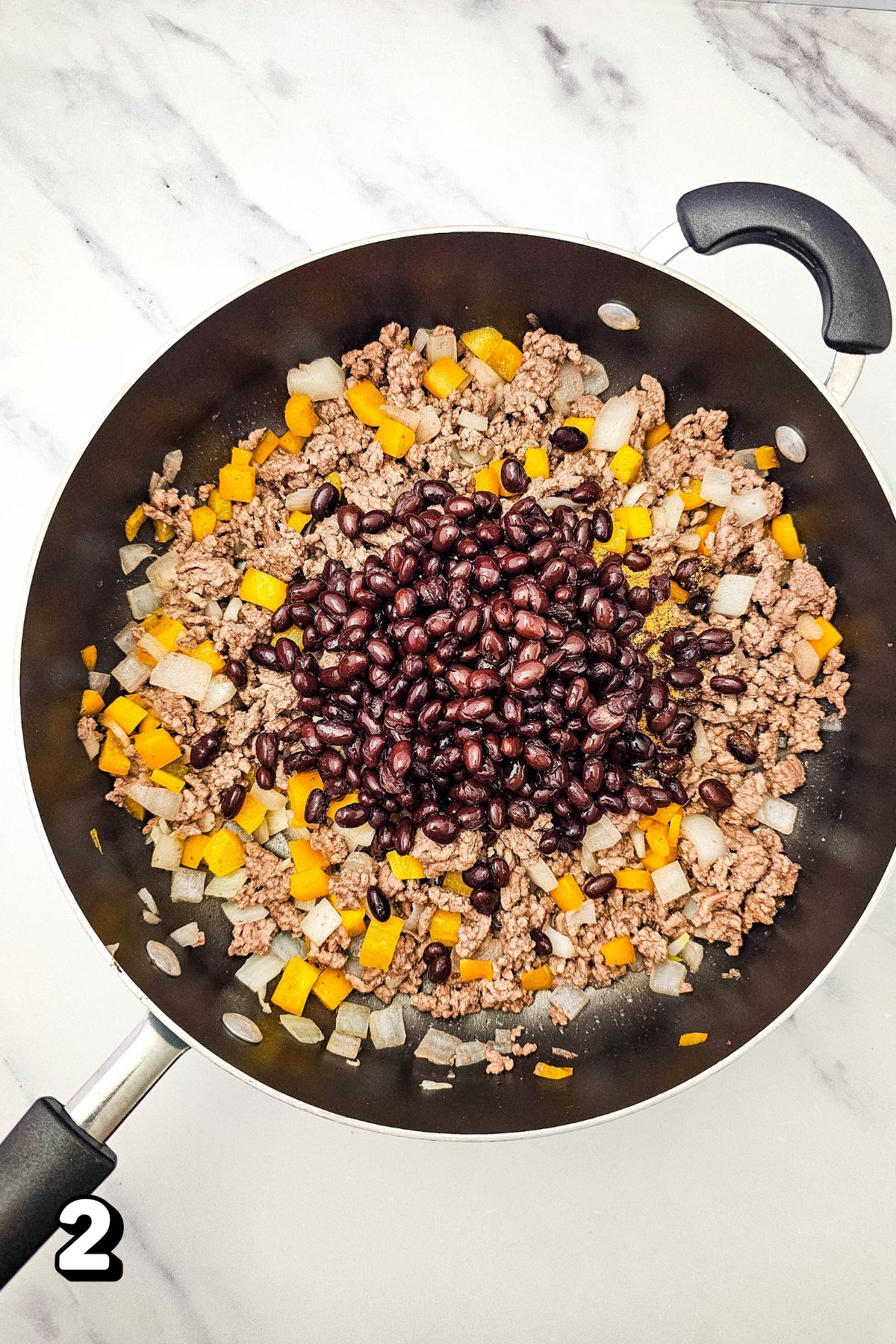 Black beans with ground beef, onions, and peppers in a skillet.