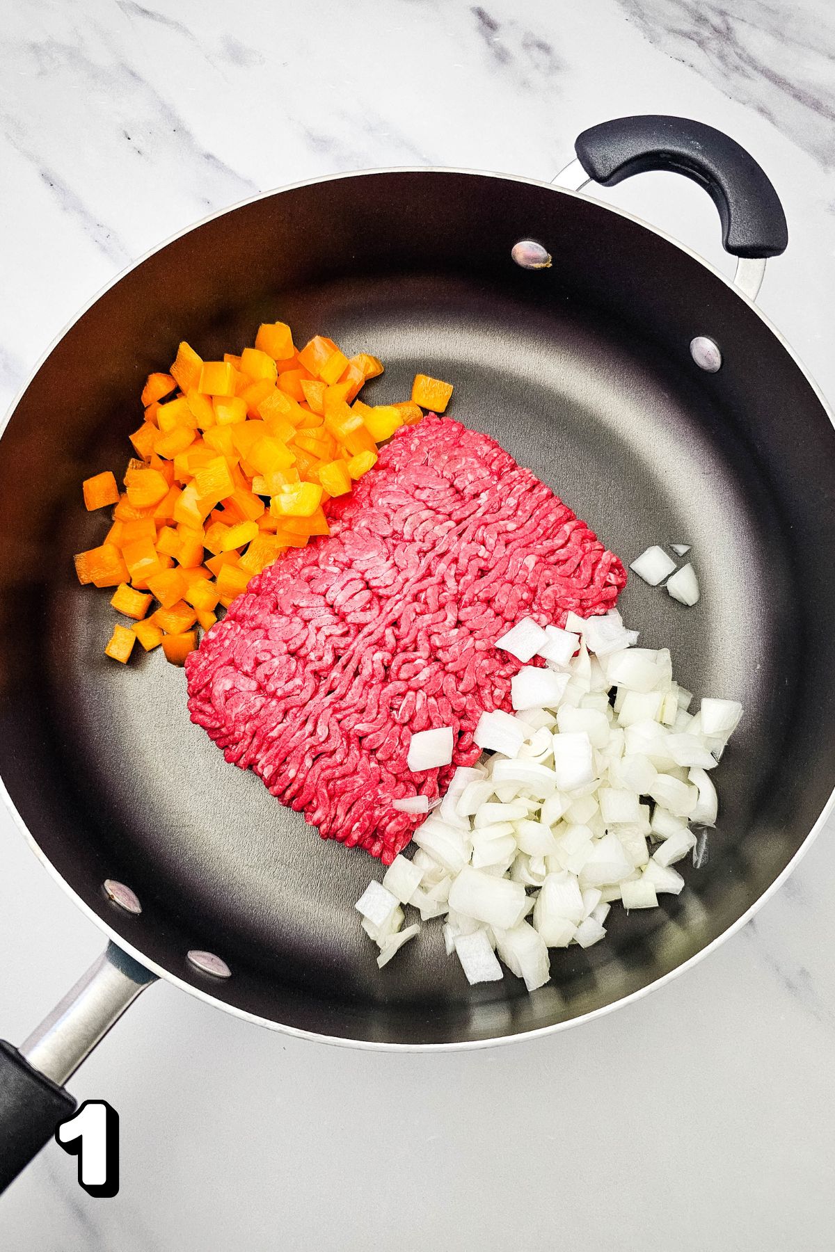 Raw ground beef with yellow peppers and onions in a skillet.