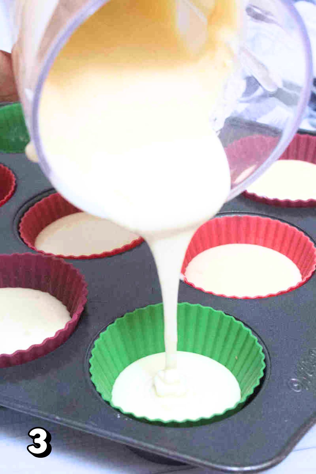 Raw blended muffin batter being poured into a lined muffin tin.