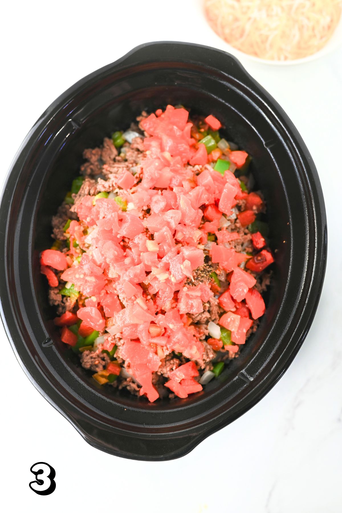 Slow cooker with tomatoes, green peppers, and ground beef in it.