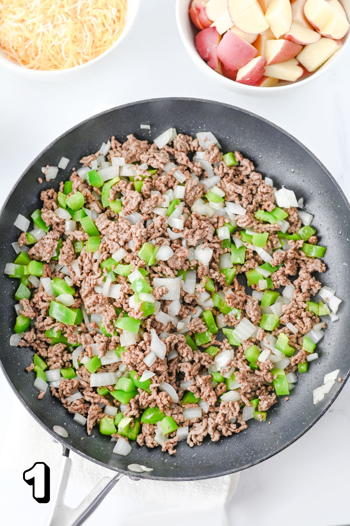 Skillet with ground beef, green peppers, and onions in it.