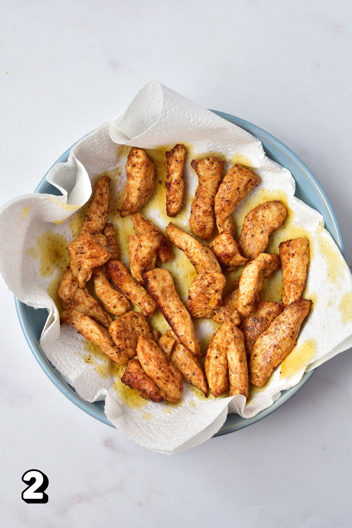 Cooked chicken strips on a paper towel lined plate.